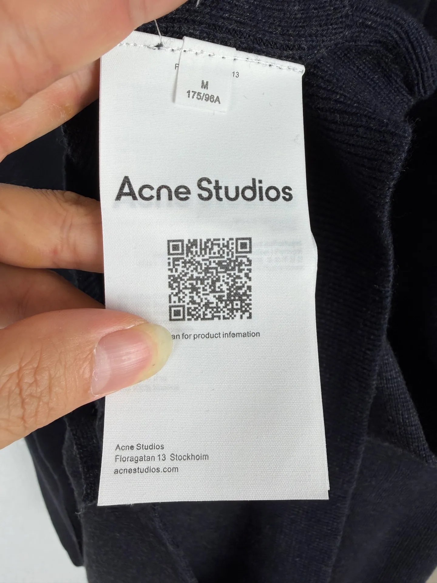 ACNE Studios black V-neck metallic round label wool cardigan sweater jacket. Ready-to-wear garments are woven from selected worsted wool blended yarns. The black-bottom mixed-color floral yarn weaving method creates a natural and delicate mottled texture through the interweaving of dark and light fibers in the yarn, which is different from ordinary plain knitted fabrics. The yarn has been pre-shrunk, smoothed and shaped in advance to control the fabric shrinkage from the source and avoid problems such as size deformation and fabric wrinkles during subsequent washing. The pattern adopts a Classic short V-neck structure. The collar curvature and placket depth are repeatedly calibrated during the pattern-making stage to ensure smooth and even lines of the V-neck. The front placket adopts an integrated woven strip structure to prevent curling and heaving during long-term wear. Four matte buttons of the same color are evenly arranged, the button positions are accurately positioned, and the sewing thread tension is consistent to ensure that the placket is straight and regular. Small metal round mark hardware is installed on the lower side of the body. The knitted fabric has strong ductility, and the alignment requirements for fixing the hardware are strict. The seam strength needs to be precisely controlled to prevent holes and local stretch deformation from being pulled by the fabric. The cuffs, hem and collar are equipped with a same-density rib structure. The rib elasticity and yarn count match the main body of the garment to achieve stable rebound after stretching and not easy to loosen. The entire garment uses smooth overlocking technology, and the inner seams are smooth and smooth to reduce skin friction and irritation. After the sewing process is completed, steam setting is done in different areas, and the V-neck, placket, and hem are ironed with controlled temperature in different areas. Knitted fabrics are prone to aurora hot stamping, so ironing operations require a spacer and strict control of steam temperature and ironing time to maintain the original matte texture of the fabric. Knitted fabrics have strong plasticity and low error tolerance in the production process. Yarn weaving, piece stitching, hardware assembly, and garment shaping are all closely linked. Any deviation in process parameters will destroy the overall silhouette. A large number of fine details are difficult to achieve high-speed processing on the assembly line. It relies on precision operations to control the details and superimpose multiple processes to create a simple and advanced basic knitted single with a sense of quality. Size:XS S M L
